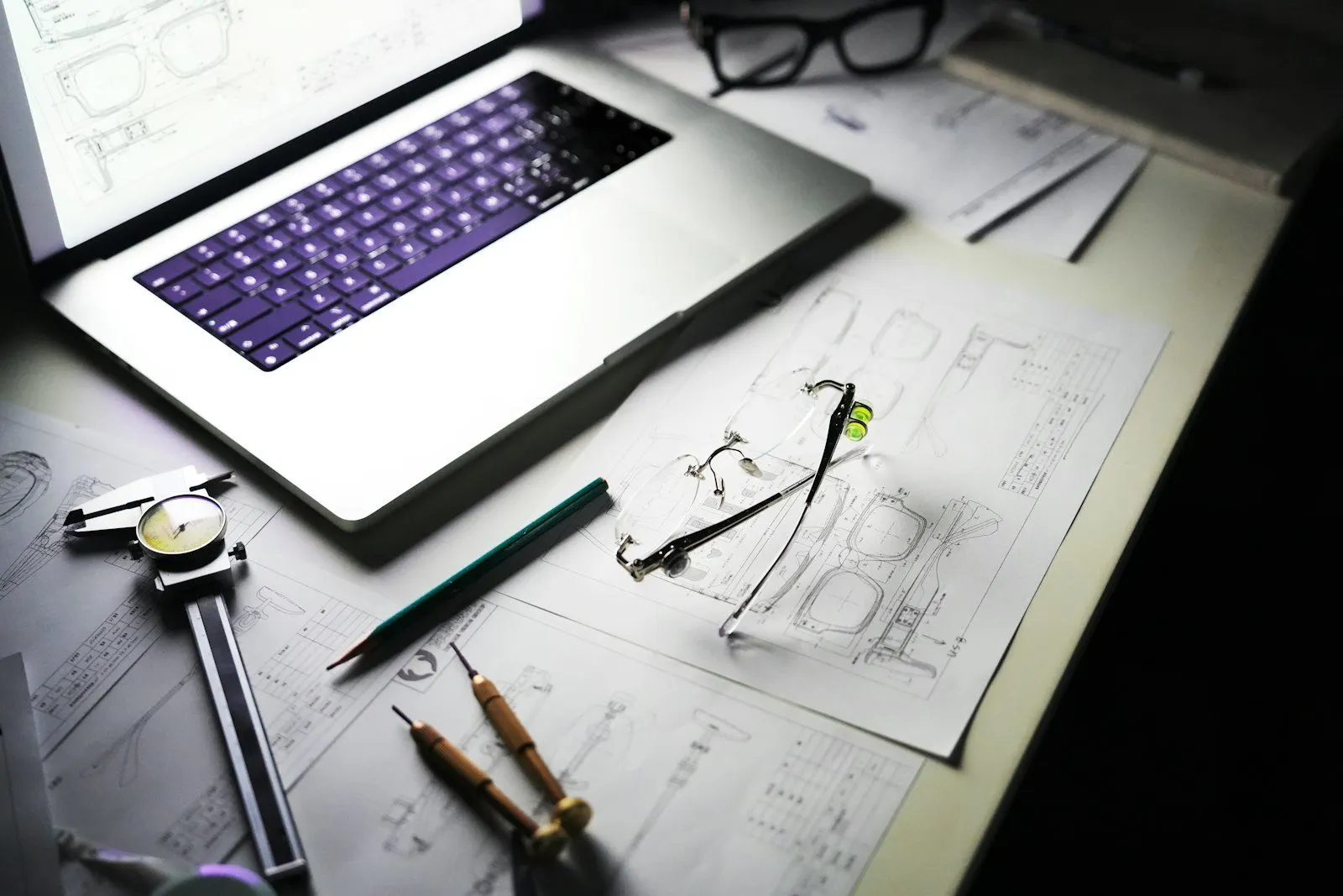 Mesa de trabajo con planos mecánicos, instrumentos de medición y una computadora portátil
